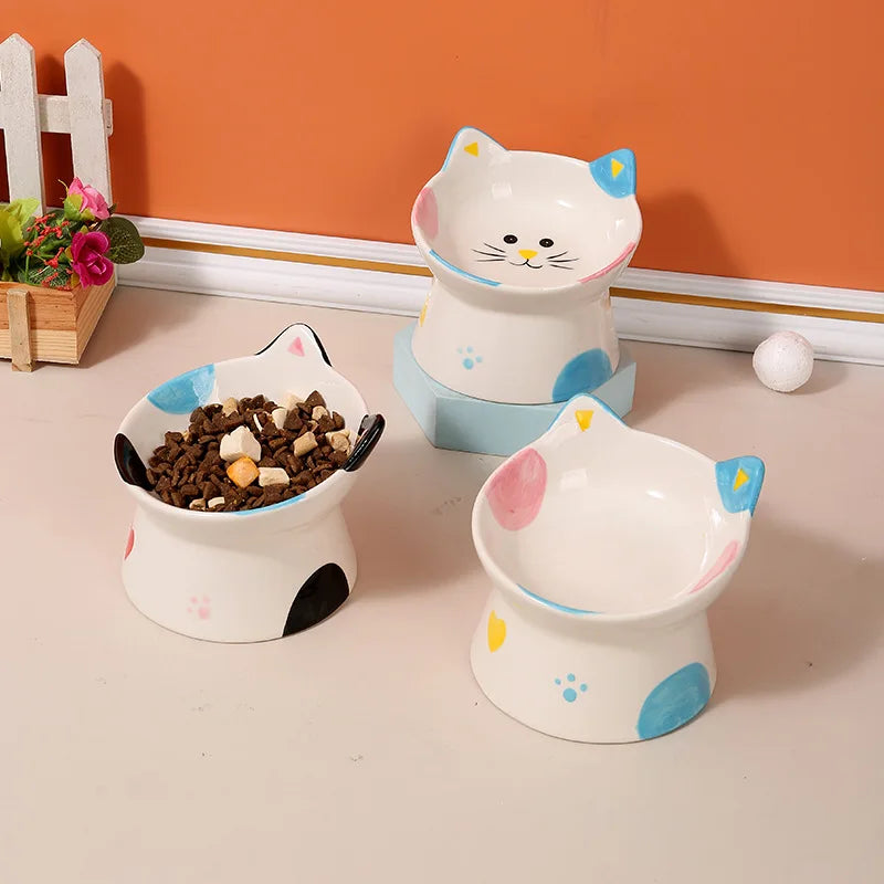 Two cat-face ceramic bowls, one with food, on a wooden floor