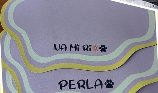Two purple personalised feeding mats with yellow and cream wavy borders